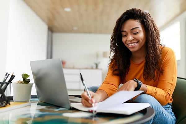 Smiling woman taking notes in front of laptop